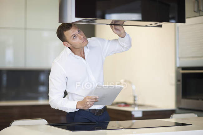 Homem adulto médio que inspeciona o capuz do extrator no showroom da cozinha — Fotografia de Stock