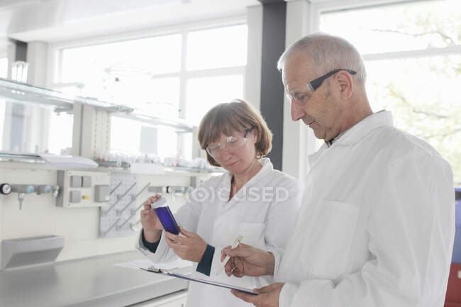 Cientistas que trabalham em laboratório, olhando para o líquido azul no frasco para injetáveis — Fotografia de Stock