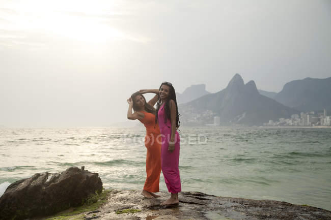 Retrato de dos mujeres jóvenes de pie sobre roca, playa de Ipanema, Río de Janeiro, Brasil - foto de stock