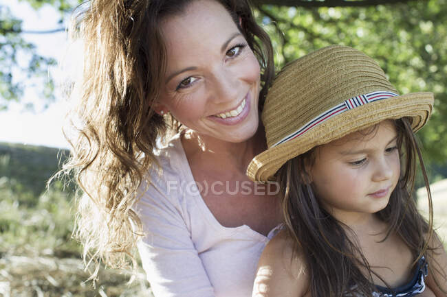 Retrato de mujer madura y su hija con sombrero de paja en el parque - foto de stock
