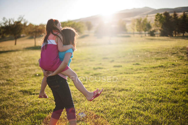Girl carrying friend piggyback in field — Stock Photo