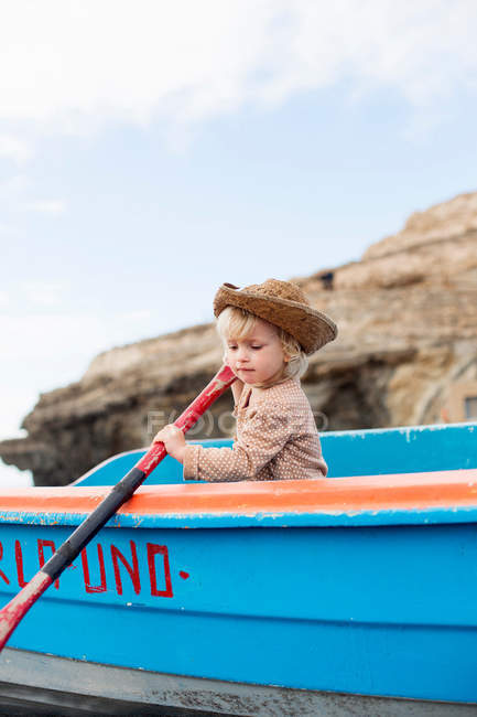 Menina criança em chapéu de palha sentado em barco a remo na praia — Fotografia de Stock