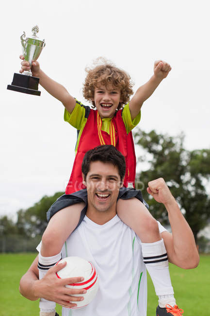 Entrenador llevando niño con trofeo - foto de stock