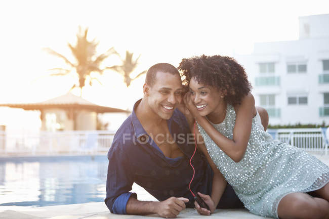 Casal elegante compartilhando fones de ouvido na beira da piscina, Rio De Janeiro, Brasil — Fotografia de Stock
