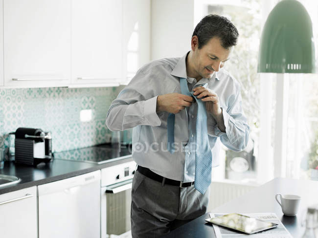Зрелый бизнесмен готовится и использует планшет на кухне — стоковое фото