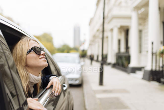 Young woman wearing sunglasses looking up from car window, London, England, UK — Stock Photo