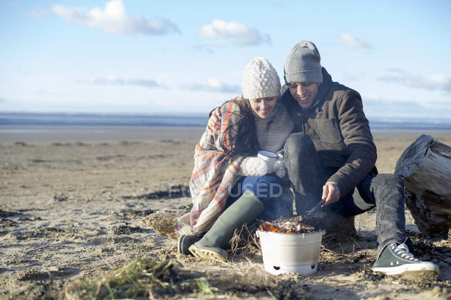 Parejas jóvenes haciendo barbacoa en la playa, Brean Sands, Somerset, Inglaterra - foto de stock