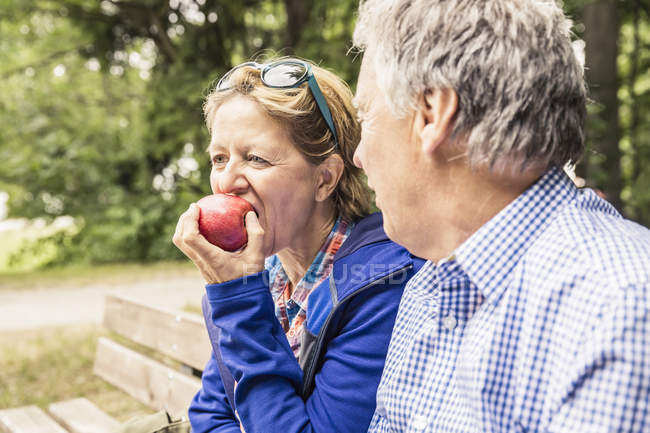 Пара сидящих на улице, зрелая женщина ест яблоко — стоковое фото