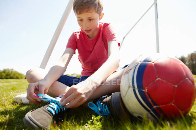 Menino sentado no campo amarrando laço de sapato — Fotografia de Stock