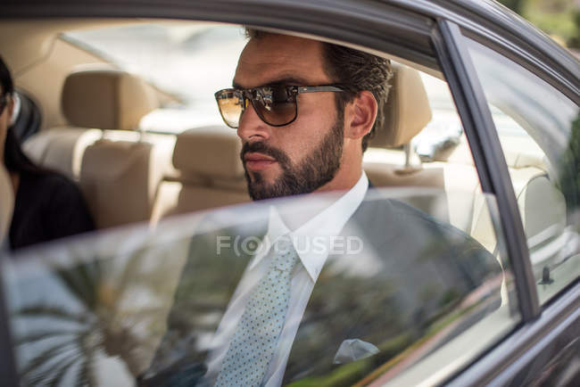 Jovem empresário usando óculos de sol no banco de trás do carro, Dubai, Emirados Árabes Unidos — Fotografia de Stock