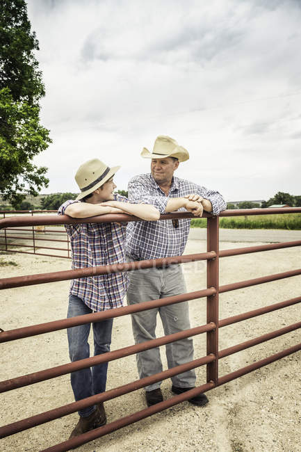 Farmer and teenage grandson leaning against gate chatting — Stock Photo
