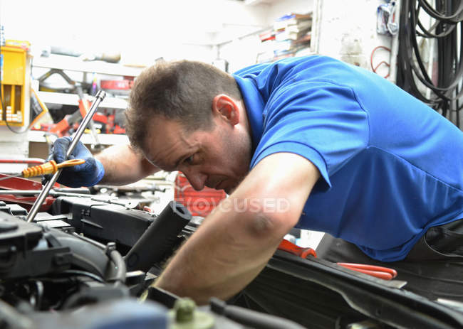 Механик среднего возраста, проверяющий двигатель автомобиля — стоковое фото