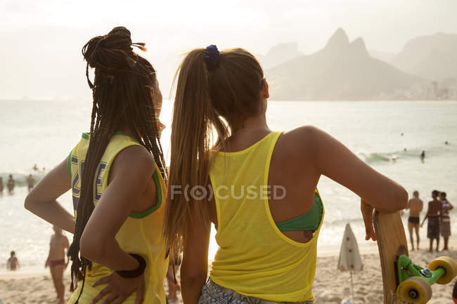 Vista trasera de dos mujeres jóvenes con vistas a la playa de Ipanema, Río de Janeiro, Brasil - foto de stock