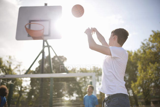 Joven jugador de baloncesto masculino lanzando baloncesto en aro - foto de stock