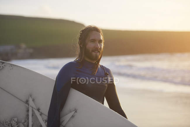 Портрет молодого серфера, несущего доску для серфинга на пляже, Девон, Англия, Великобритания — стоковое фото