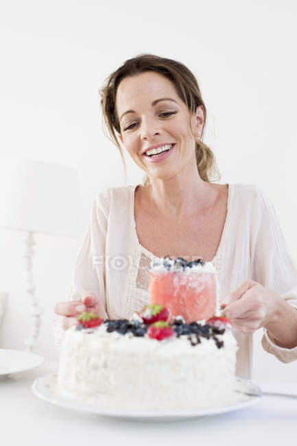 Mujer madura sirviendo pastel cubierto de frutas mirando hacia abajo sonriendo - foto de stock