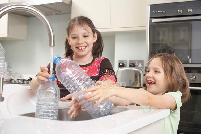 Ragazze che riempiono bottiglia d'acqua in cucina — Foto stock
