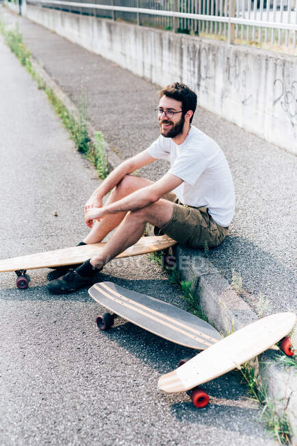Young man sitting on kerb with three skateboards — Stock Photo