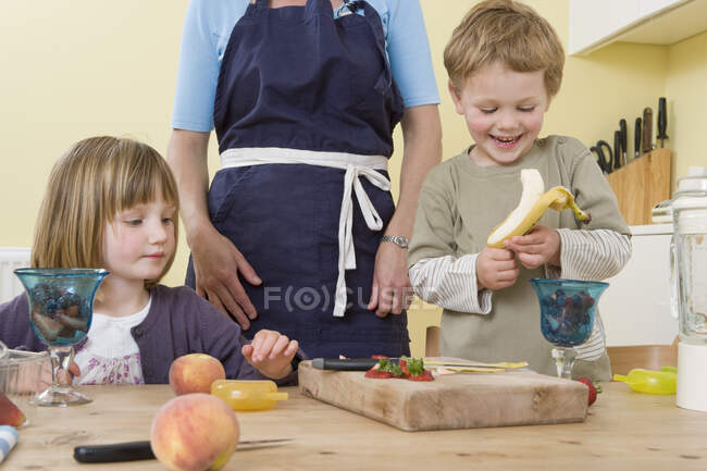 Niño, niña y madre preparando fruta - foto de stock