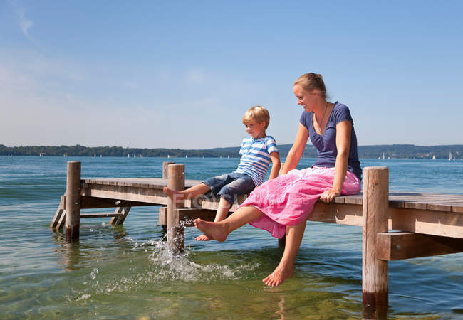 Madre e hijo sumergiendo los pies en el lago - foto de stock