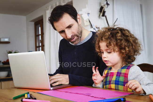 Fille dessin à la table tandis que père en utilisant un ordinateur portable — Photo de stock