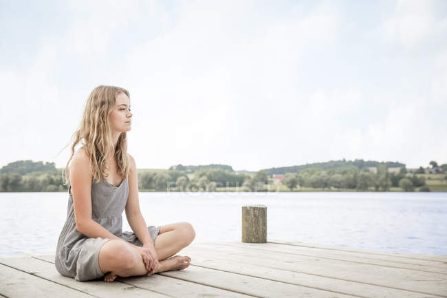 Portrait of young woman sitting on jetty, crossed legs — Stock Photo