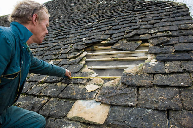 Roofer measuring hole in traditional stone tile roof — Stock Photo