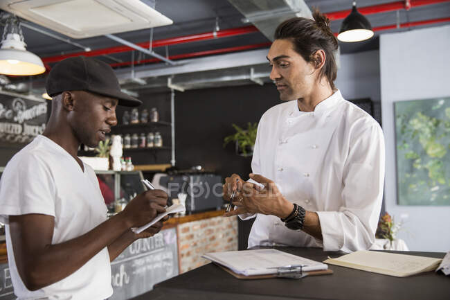 Employee in restaurant talking with chef, making notes in notebook — Stock Photo