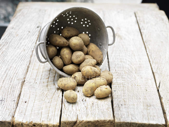 Bodegón de Jersey Royal Potatoes en colador sobre mesa de madera - foto de stock