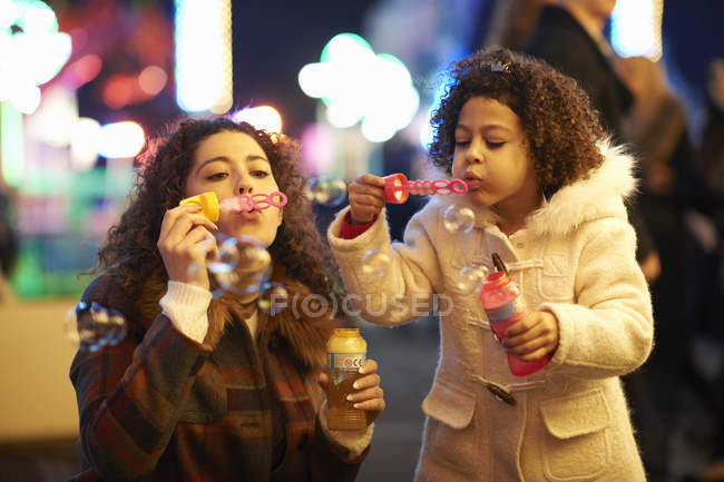 Madre e hija soplando burbujas, en la feria - foto de stock