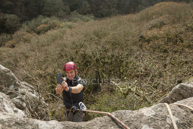 Male rock climber taking photo with smartphone — Stock Photo