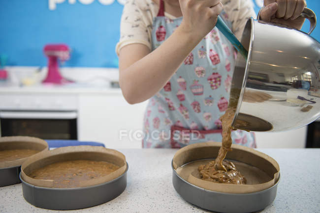 Female hands pouring mixture into cake tins in bakery — Stock Photo