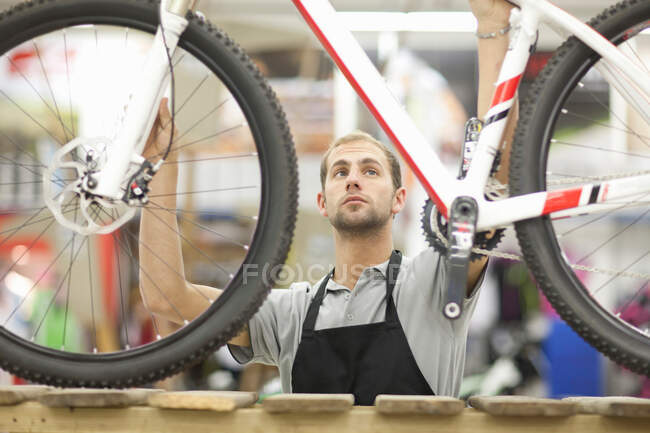 Joven sosteniendo bicicleta en taller de reparación - foto de stock
