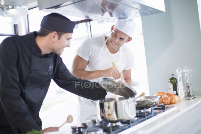 Dois chefs masculinos cozinhando na placa na cozinha comercial — Fotografia de Stock