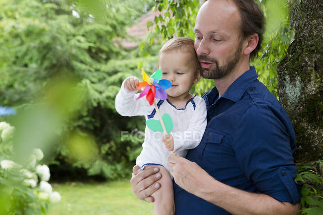 Pai e bebê filha brincando com pinwheel no jardim — Fotografia de Stock