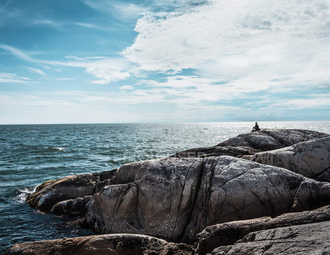 Person sitzt auf Felsformation an der Küste — Stockfoto