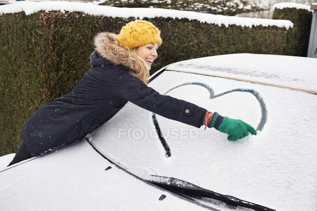 Frau zeichnet Herzform auf verschneite Windschutzscheibe — Stockfoto