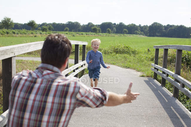 Chico corriendo sobre puente de madera hacia papá - foto de stock