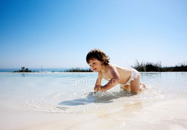 Baby crawling in water on the beach — Stock Photo