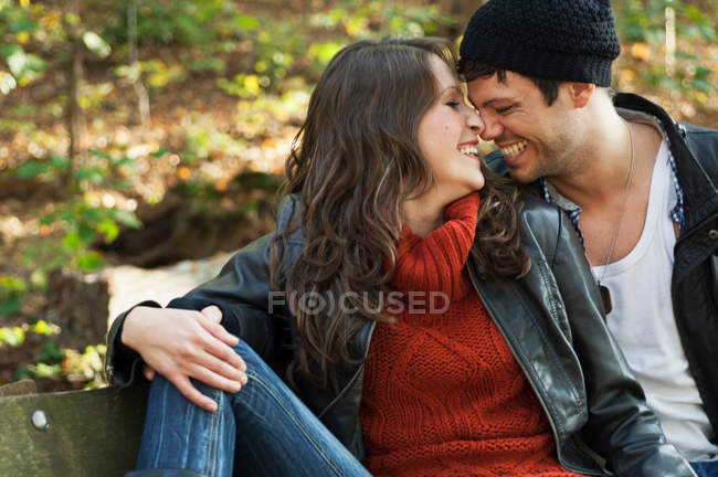 Portrait of couple nuzzling on bench in autumnal park — Stock Photo
