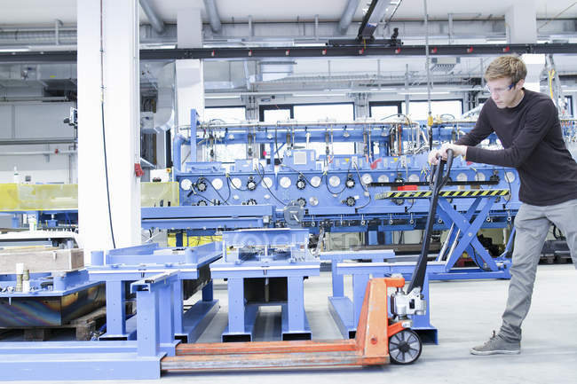 Mid adulto masculino movendo produtos em paletes jack na planta de engenharia — Fotografia de Stock