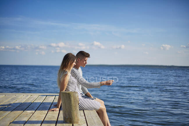 Пара сидить на дерев'яному пірсі, дивлячись на — стокове фото