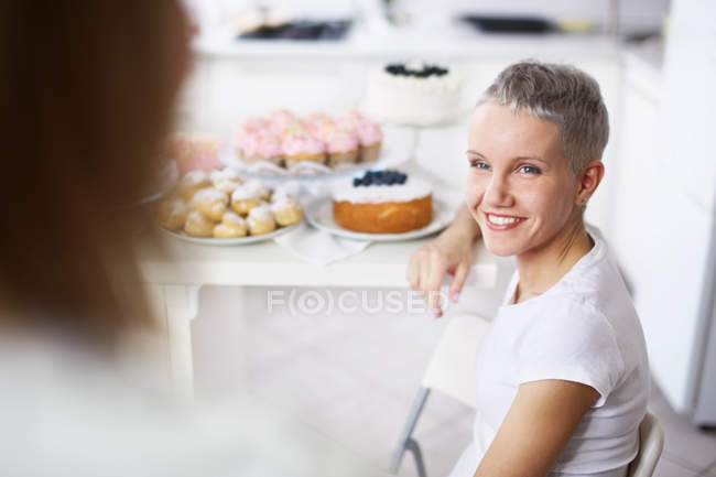 Two women talking with cakes at background — Stock Photo