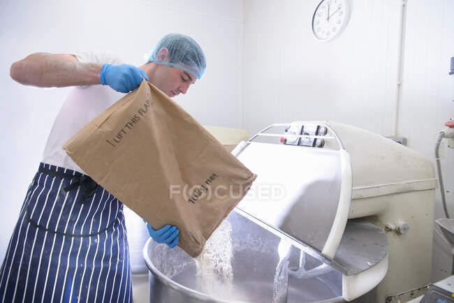 Пекарь наливает муку из мешка в смеситель — стоковое фото