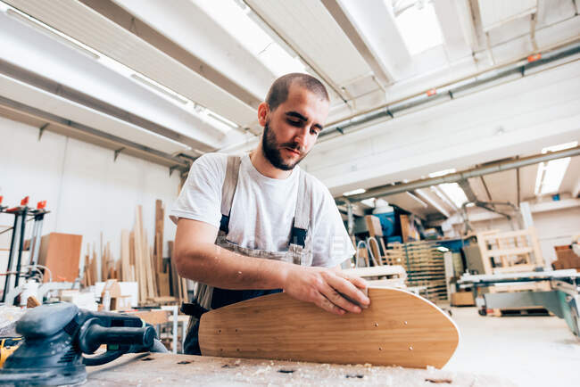 Young man in carpentry workshop looking down sanding skateboard — Stock Photo