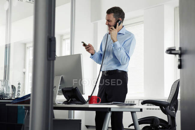 Mature businessman on landline phone in office — Stock Photo