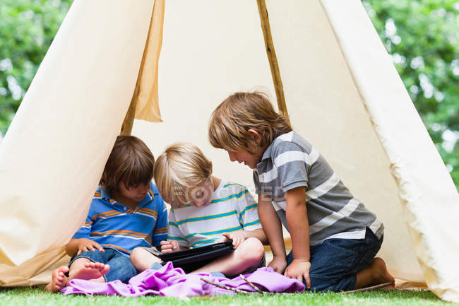 Boys using tablet computer in tent — Stock Photo