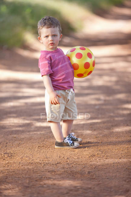 Tout-petit garçon avec balle sur la route de terre — Photo de stock