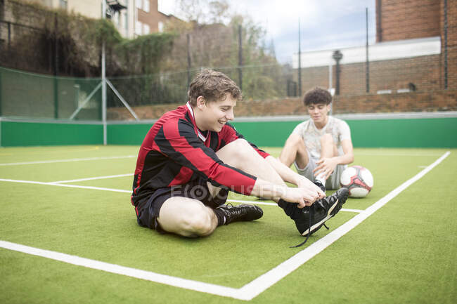 Two young men on urban football pitch, tying shoelaces — Stock Photo