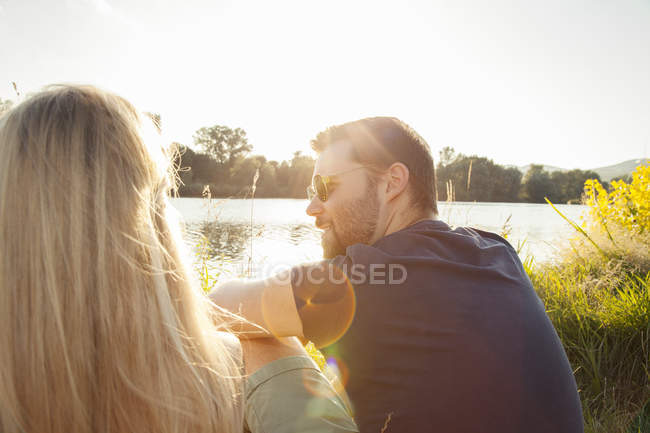 Jovem casal sentado na margem do rio à luz do sol — Fotografia de Stock